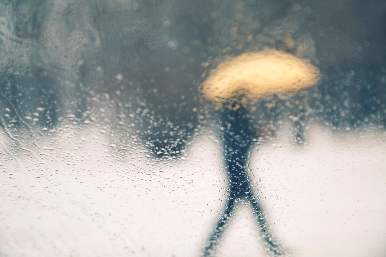 Abstract blurred snowy and rainy person walk with yellow umbrella. View from rainy car glass window. Conceptual bad weather background.